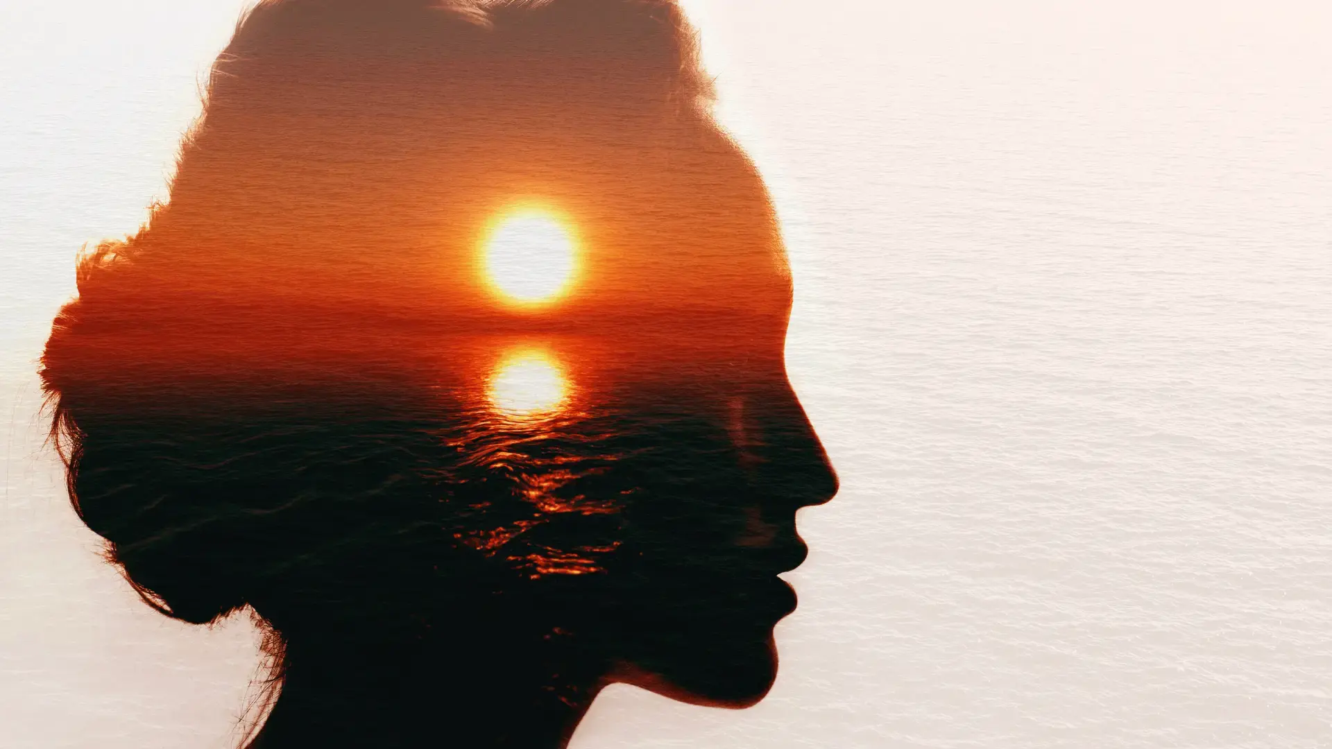 Double exposure photograph of a person's silhouette in profile blended with an ocean sunset, with the sun and its reflection visible within the figure