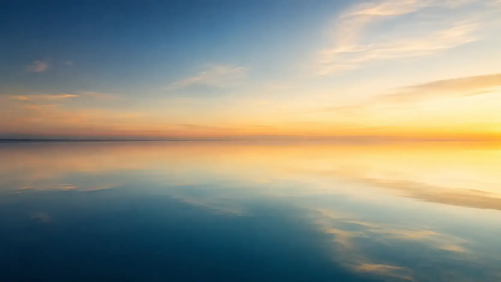 Still water holding a soft, calm reflection of open sky at dawn, in muted navy, teal, and gold tones