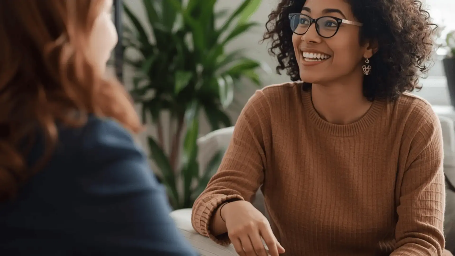 Two women in a warm, engaged conversation in a professional setting with a green plant in the background
