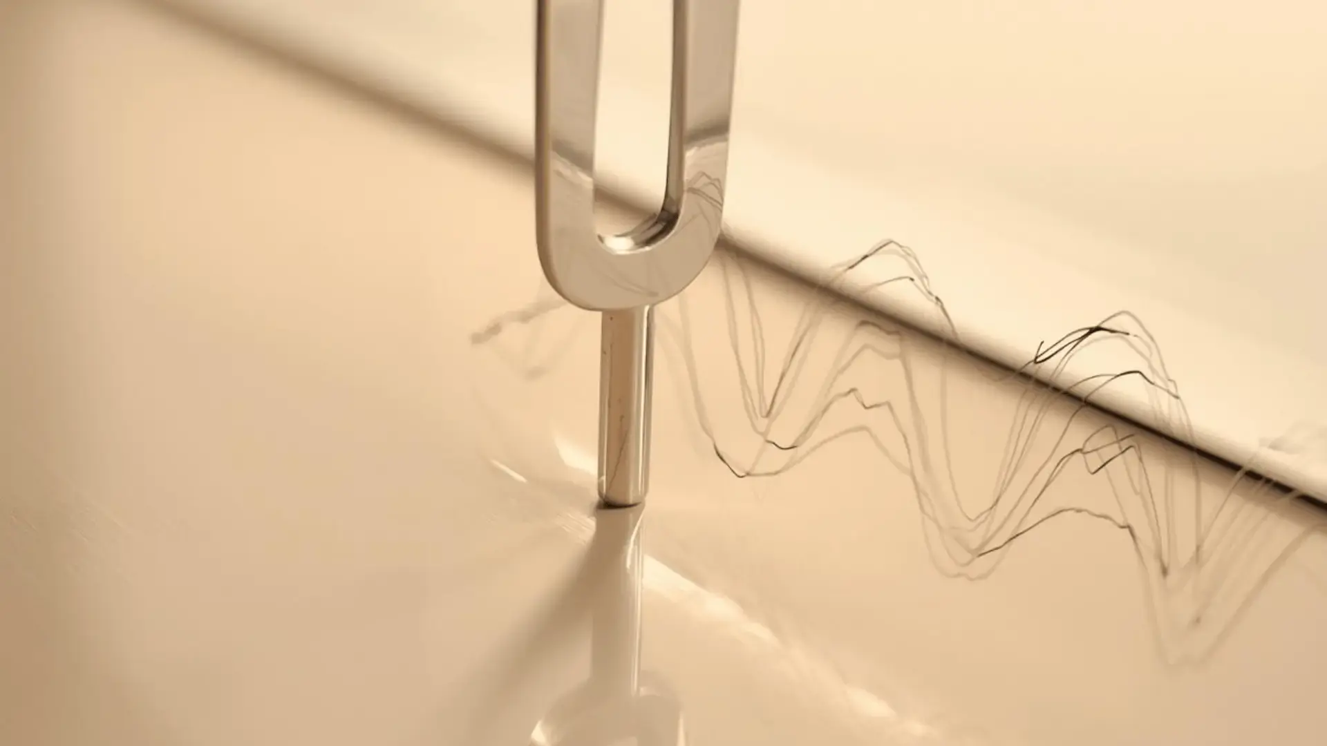 Close-up of a tuning fork vibrating on a smooth surface, with visible sound wave patterns radiating outward in warm golden light Trauma Therapist Institute