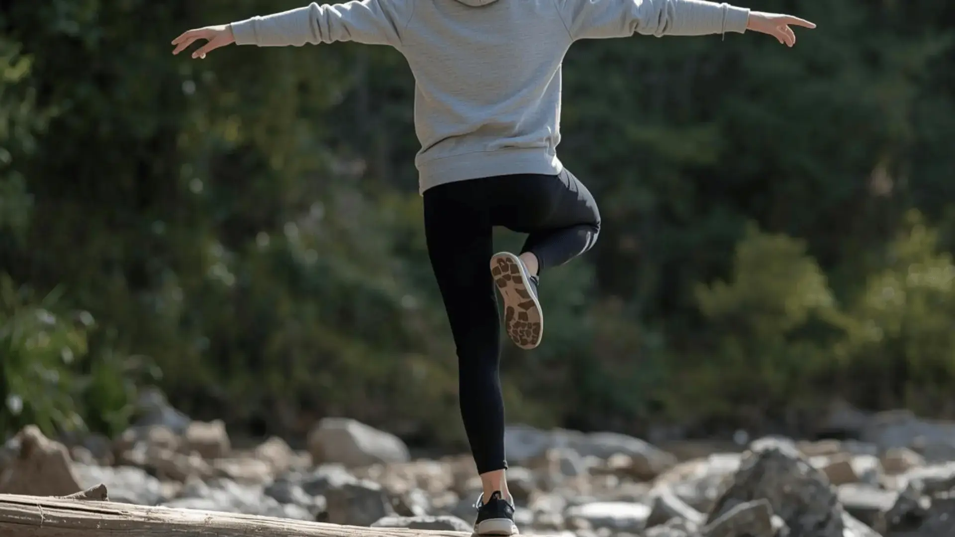 Person balancing on one foot on a log outdoors with arms outstretched, seen from behind in a rocky natural setting Trauma Therapist Institute