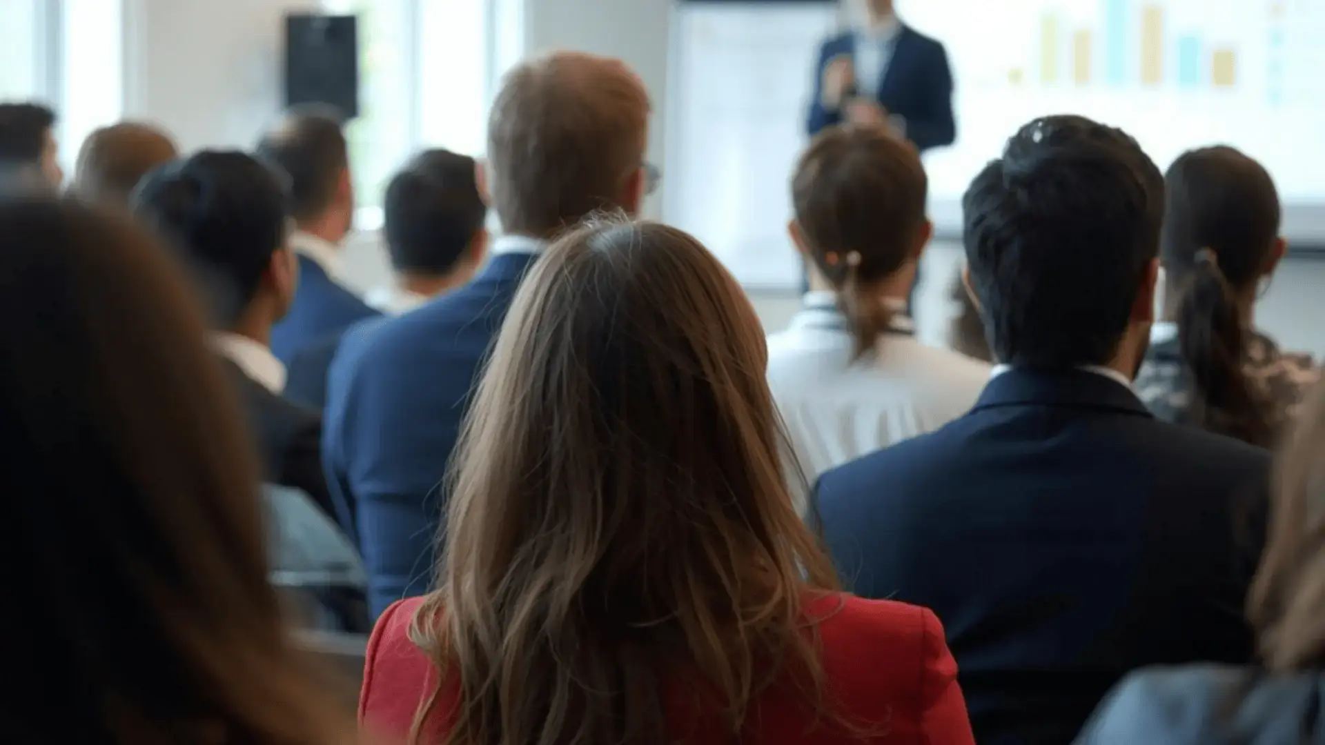 Professionals attending a training session, seen from behind, facing a presenter at a whiteboard in a bright conference room Trauma Therapist Institute