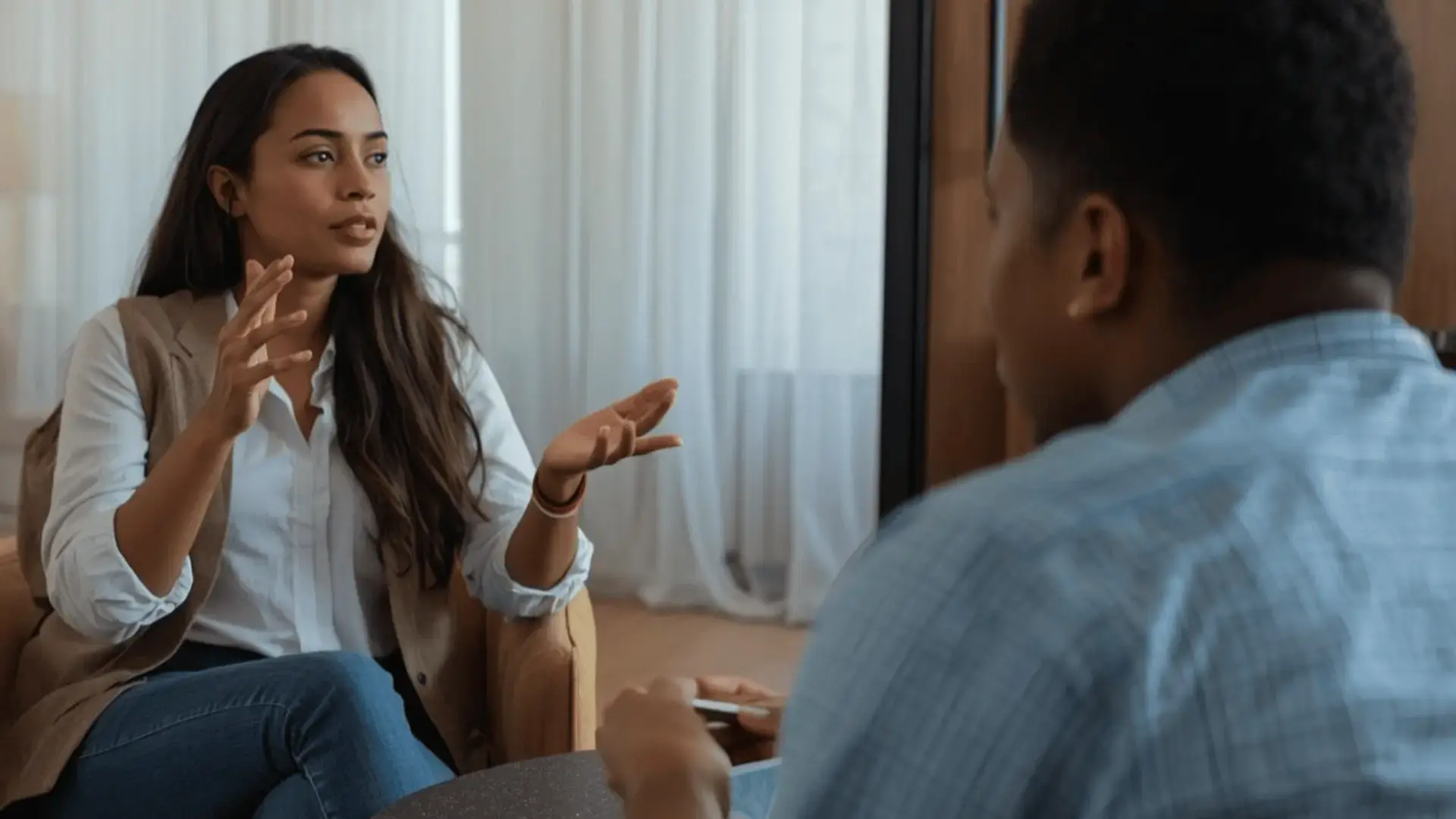 Therapist gesturing while explaining a concept to a client during a session in a warm, naturally lit room Trauma Therapist Institute